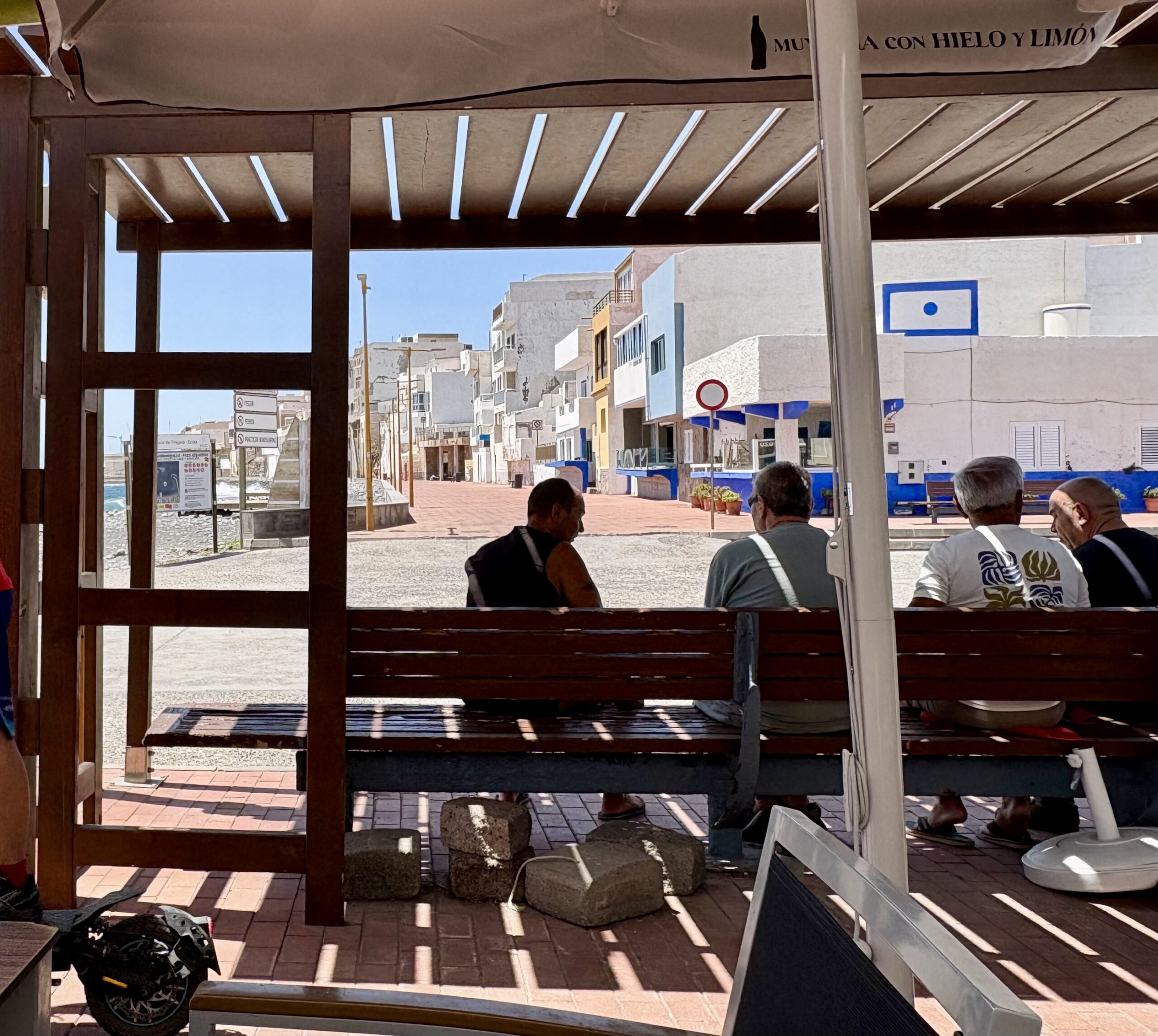 Menschen sitzen im Schatten mit Blick auf die einfachen Häuser von Pozo Izquierdo