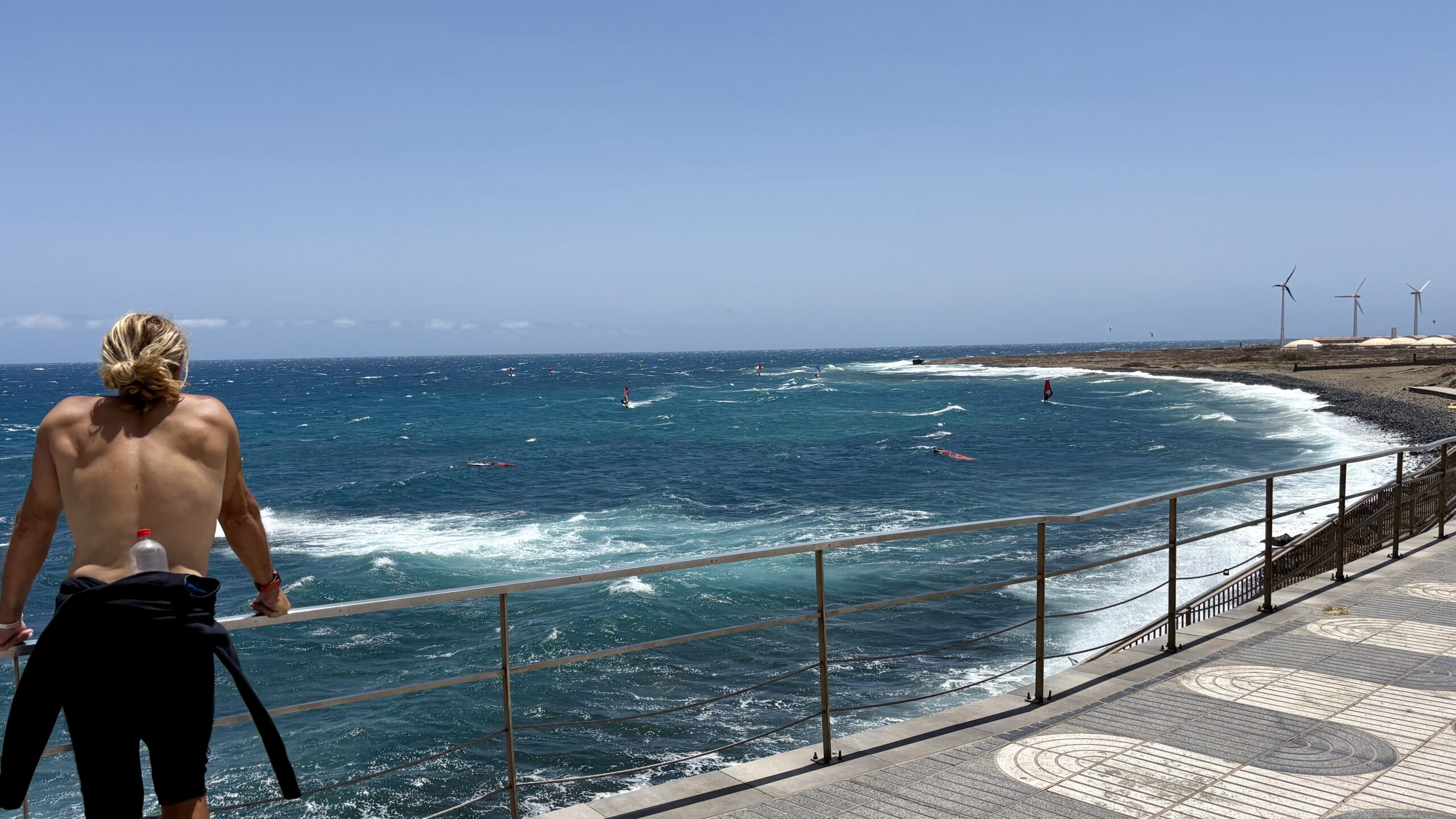 Surfer blickt in Pozo Izquierdo auf den windigen Atlantik mit Windsurfern und Windrädern
